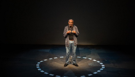 Tyrone stands in the middle of the circle of cards on the floor looking thoughtful
