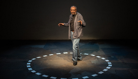 Tyrone stands in the middle of the circle of cards on the floor with his arms outstretched in motion